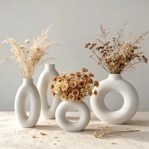 Detailed view of four minimalist white donut-shaped resin vases with dried flowers