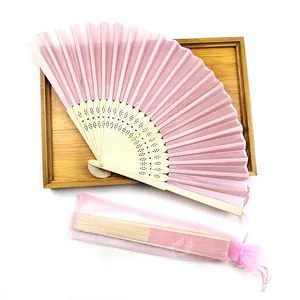 Detailed view of pink silk folding fan set with organza gift bag on a wooden tray background