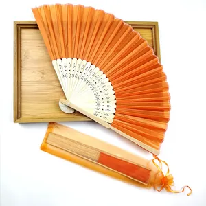 Detail view of orange folding fan set with matching organza gift bag on wooden tray
