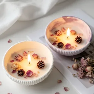 Close-up of DIY scented candles in fluted bowls decorated with dried flowers and pine cones