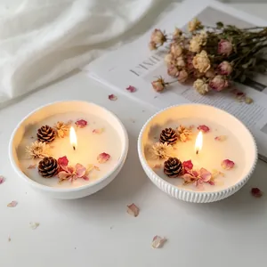Close-up of handmade white candle bowls decorated with dried flowers and pine cones.