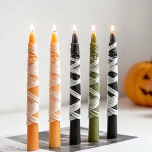 Close-up of five lit Halloween mummy taper candles in various festive colors