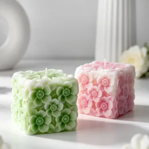 Dettaglio di candele decorative a cubo con trame floreali a rilievo in verde e rosa