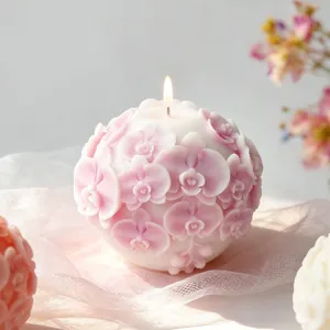 Detailed view of a lit embossed orchid flower ball scented candle with delicate pink petals