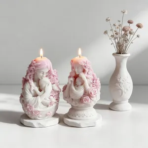 Detailed view of two lit pink and white mother and baby sculpted candles with flowers.