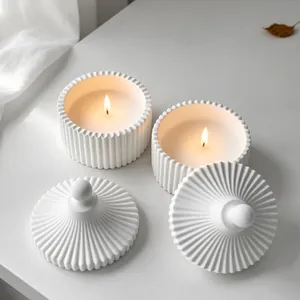 Primer plano de velas aromáticas encendidas en tarros de yeso estriado con tapas.