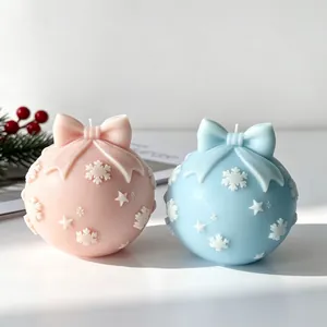 Detailopname van roze en blauwe kerstbalgeurkaarsen met sneeuwvlokken en een strik.