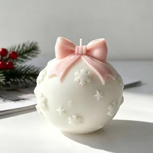 Detailweergave van een witte kerstkaars met roze strik en reliëf van sneeuwvlokken.
