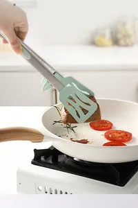 Detailed view of heat-resistant silicone food tongs flipping a juicy steak in a frying pan