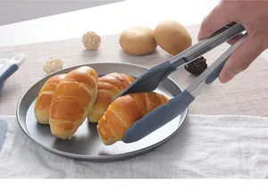 Stainless steel silicone food tongs picking up a fresh croissant in a kitchen setting.