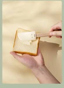 Cute smiley face silicone spatula spreading cream on toast bread, baking tool detail view