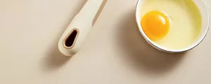 Close-up detail of a cream silicone whisk handle and a fresh raw egg in a bowl