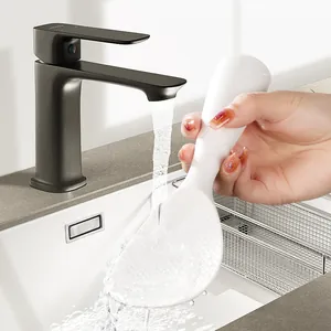 Standing white silicone rice ladle being rinsed under a kitchen faucet