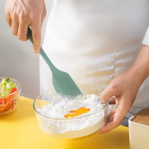 Close-up of green silicone spatula mixing eggs and flour in a glass bowl