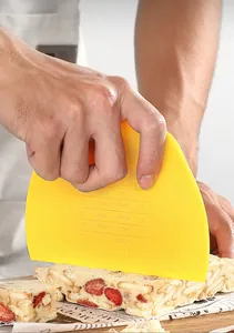 Cortador de masa de plástico amarillo con medidas grabadas cortando turrón de fresa