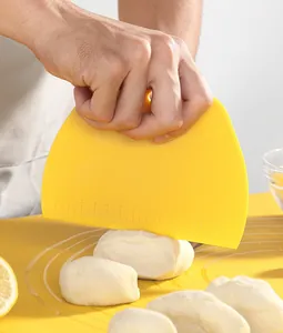 Primer plano de un raspador de masa de plástico amarillo con medidas cortando masa fresca.