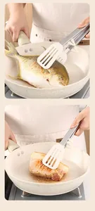 Stainless steel and silicone kitchen tongs flipping fish and meat in a non-stick pan