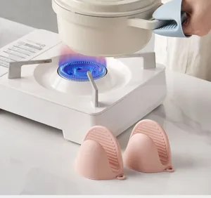 Close-up of a person using a blue heat-resistant silicone oven mitt to lift a white hot pot
