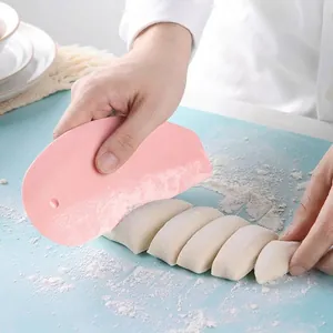 Pink plastic dough scraper and cutter on blue silicone pastry mat for home baking