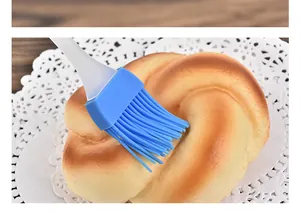 Close-up of a blue silicone basting brush being used on a freshly baked golden brown bun.