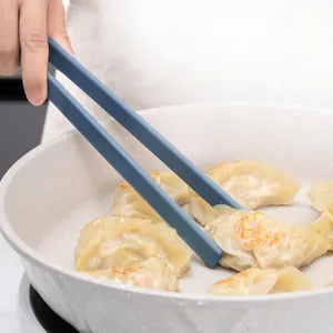 Professional blue food-grade silicone cooking tongs flipping dumplings in a non-stick pan