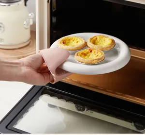 A pink heat resistant silicone oven mitt holding a hot ceramic plate with egg tarts