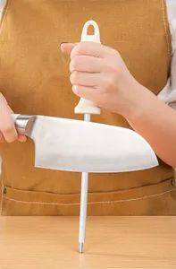 Detail showing a manual stainless steel sharpening rod honing a professional kitchen knife
