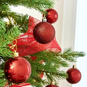 Close-up of red glitter and shiny Christmas baubles hanging on a pine tree branch.