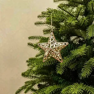 Detailed view of a golden hollowed star ornament hanging on a lush green Christmas tree.