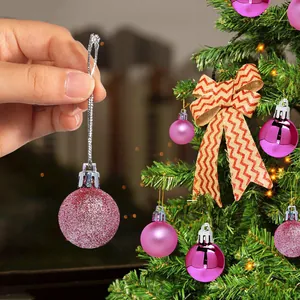 Detailed close-up of a pink glitter Christmas bauble held by hand against a festive tree