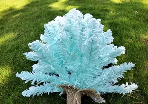 Vue détaillée d'un sapin de Noël floqué bleu clair avec effet neige réaliste sur herbe.