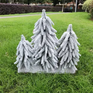 Detailansicht von drei beflockten Mini-Weihnachtsbäumen mit Schneeeffekt im Gras