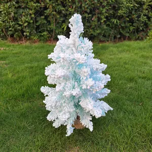 Gros plan d'un sapin de Noël bleu floqué avec une texture de neige réaliste sur l'herbe.