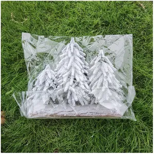 Nahaufnahme von drei kleinen verschneiten Weihnachtsbäumen in Klarsichtfolie auf grünem Gras