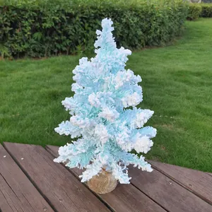 Détail d'un petit sapin de Noël bleu floqué avec effet de neige sur une terrasse en bois