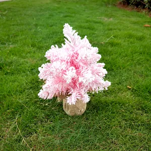 Un joli mini sapin de Noël rose floqué avec une base en toile de jute sur l'herbe verte
