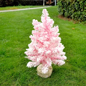 Vue détaillée d'un mini sapin de Noël rose floqué avec base en toile sur l'herbe