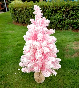 Petit sapin de Noël rose floqué avec base en toile de jute sur une pelouse verte