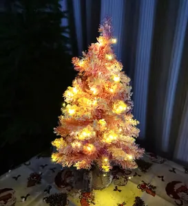 Gros plan d'un mini sapin de Noël rose floqué décoré de lumières LED jaunes chaudes