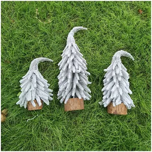 Detailansicht von drei Mini-Weihnachtsbäumen mit Holzsockel auf grünem Gras im Freien