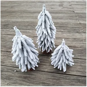 Detailansicht von drei Mini-Schnee-Weihnachtsbäumen mit Holzsockel auf einem Dielenboden.