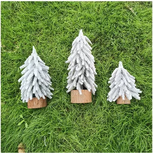 Detailansicht von drei mini beflockten Weihnachtsbäumen mit Holzfuß auf grünem Grasboden