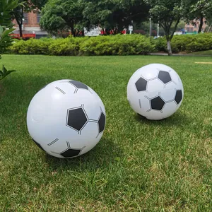 Two black and white inflatable soccer balls sitting on green grass in a sunny outdoor park.