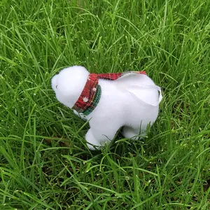 Close-up of a fuzzy white polar bear ornament with a red plaid scarf on green grass.