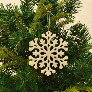 Close-up of a white glittery acrylic snowflake ornament hanging on a green Christmas tree.