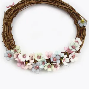 Dettaglio di una corona di vite rustica decorata con piccoli fiori di seta colorati.