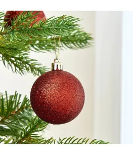 Primer plano de una bola de Navidad roja con purpurina colgada en una rama de pino
