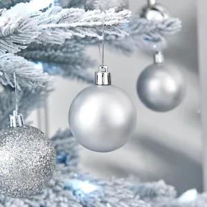 Detalle macro de bolas de Navidad plateadas en una rama de árbol nevada.