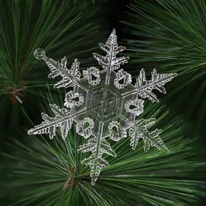 Detailansicht einer klaren Acryl-Schneeflocke an einem grünen Weihnachtsbaum aufgehängt