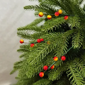 Gros plan d'une branche de baies de Noël artificielle avec des aiguilles de pin réalistes